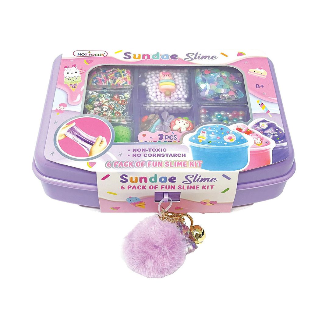 A kids' craft kit labeled 'Sundae Slime & Pack of Fun Slime Kit' in a purple plastic case with a clear lid showing organized compartments of colorful beads, glitter, and accessories. A pink fuzzy pom-pom keychain with small charms hangs in front on a white background.