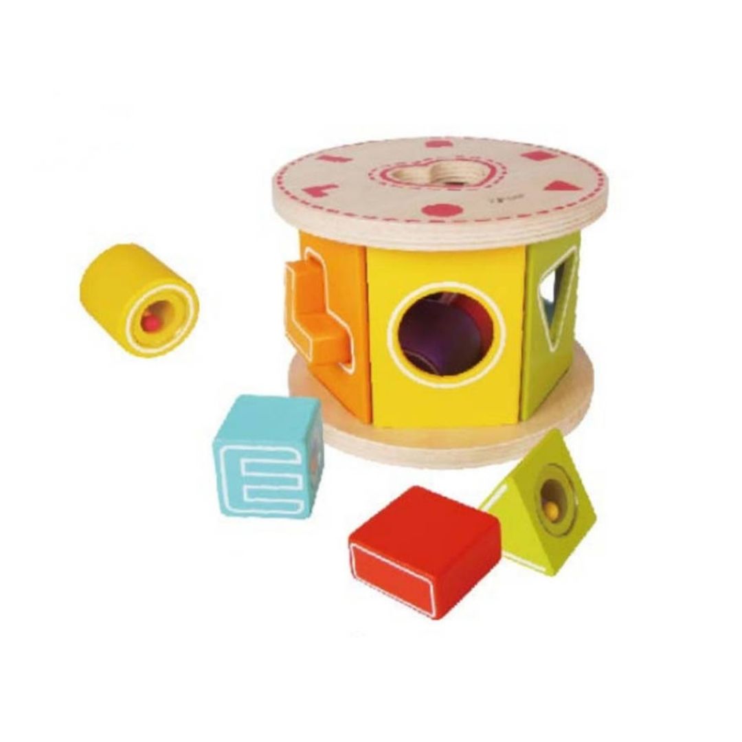 A colorful wooden shape-sorting toy set on a plain white background, featuring a cylindrical drum-shaped sorter with multiple cutouts and several loose geometric blocks in yellow, blue, red, and green.