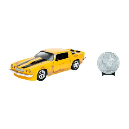 A yellow die-cast model car with black racing stripes and flame decals, shown alongside a silver commemorative coin on a small black stand against a plain white background.