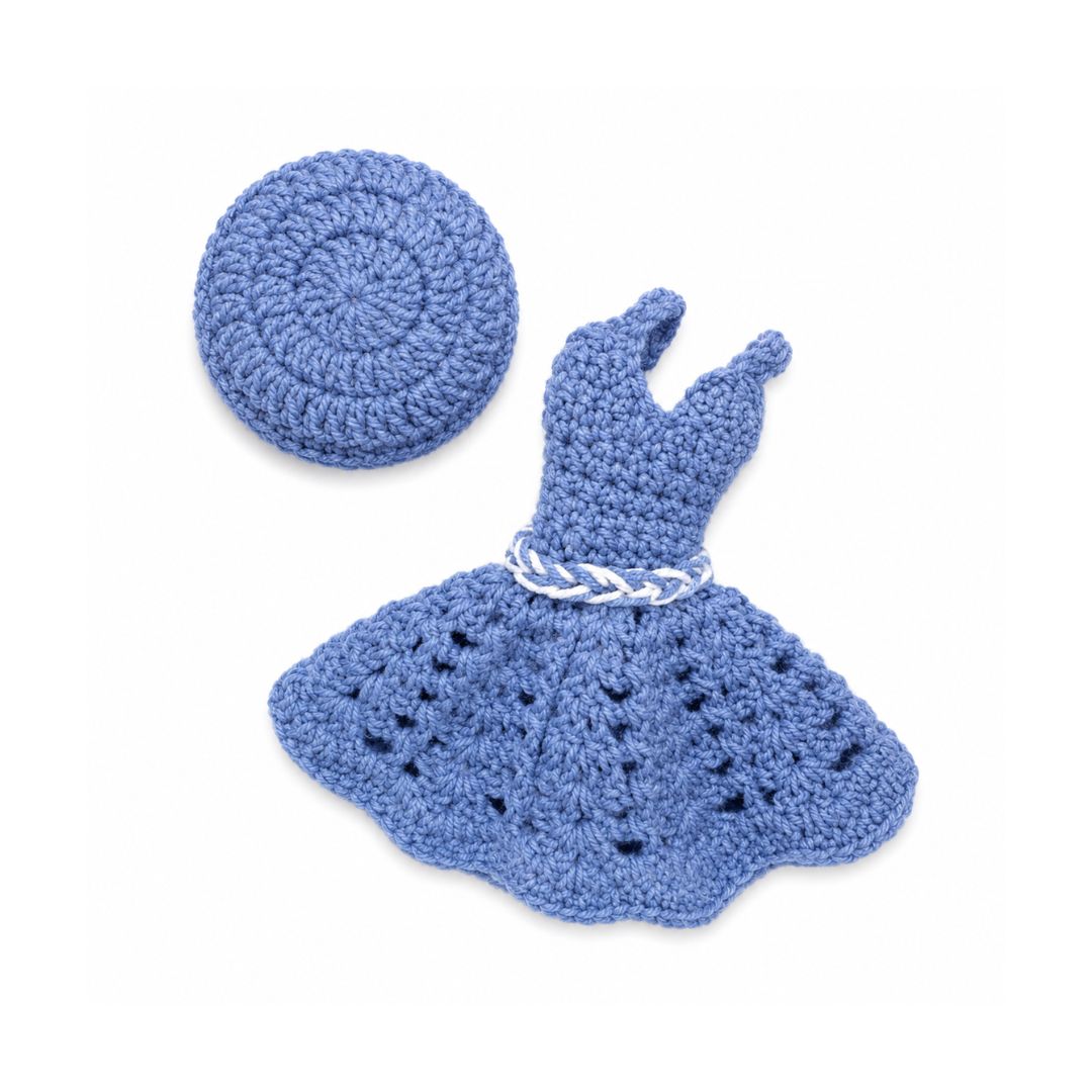 A crocheted doll outfit set in dusty blue, including a short dress with a braided white belt and a matching round hat, displayed on a clean white background.