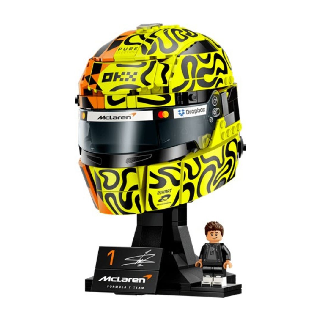 A toy building-block style helmet display featuring a yellow and black patterned racing helmet on a black stand, with a small minifigure and a plaque. Visible branding includes McLaren and Driehoek.
