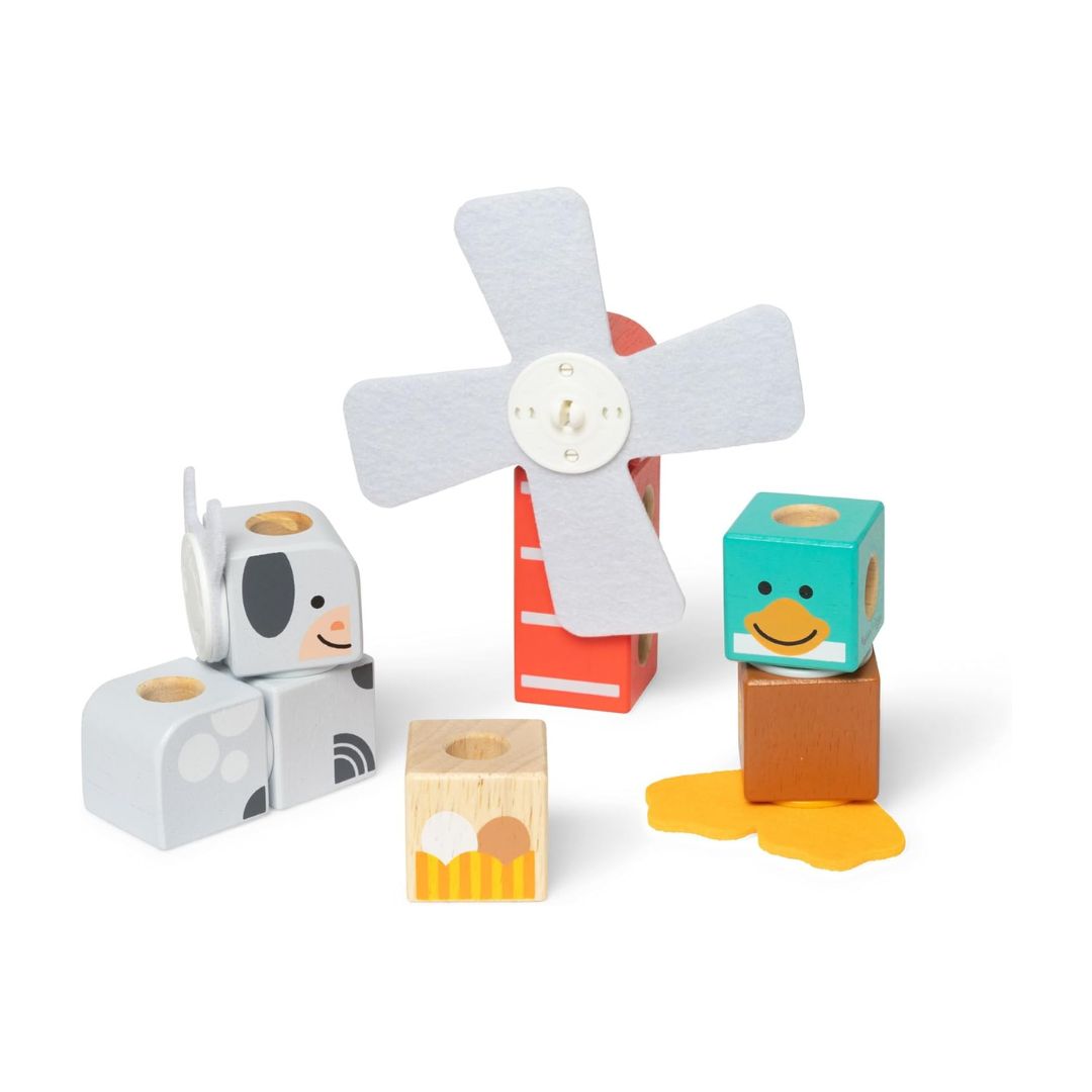 A set of wooden toy blocks and a small windmill on a clean white background. The set includes a gray cow block, a red and white ladder block, a teal duck block, a brown block, a yellow puddle block, and a small wooden farm block.