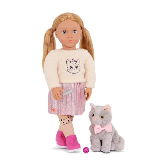 An 18-inch doll with blonde pigtails stands next to a gray plush cat toy wearing a pink bow tie. The doll is dressed in a cream fuzzy sweater with a cat face graphic, a pink glittery skirt, and pink shoes, holding a gray comb.