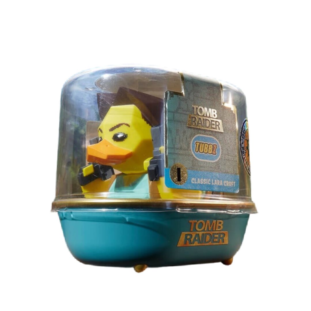A Tomb Raider Tubbz Classic Lara Croft toy figure in its original clear plastic capsule packaging, featuring a yellow duck-like figure with brown hair and a teal outfit, set against a plain white background.